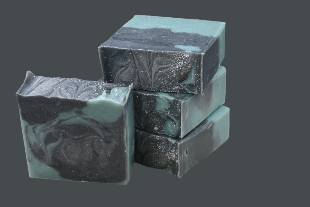 Stack of black and green soap bars on a wooden surface with a dark background