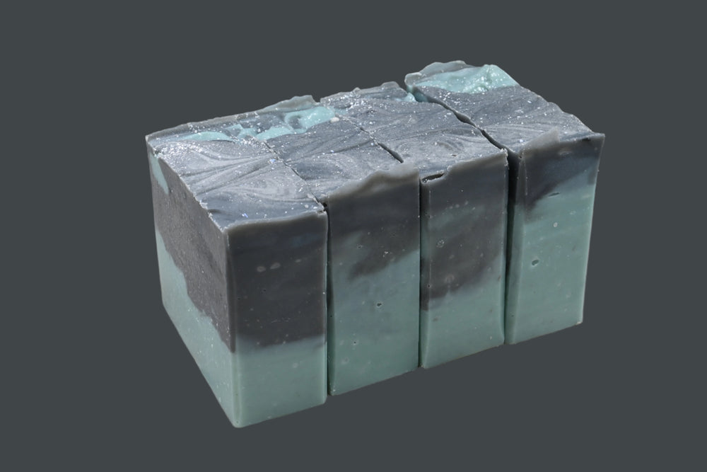 Five rectangular bars of soap stacked on a wooden surface with a dark background