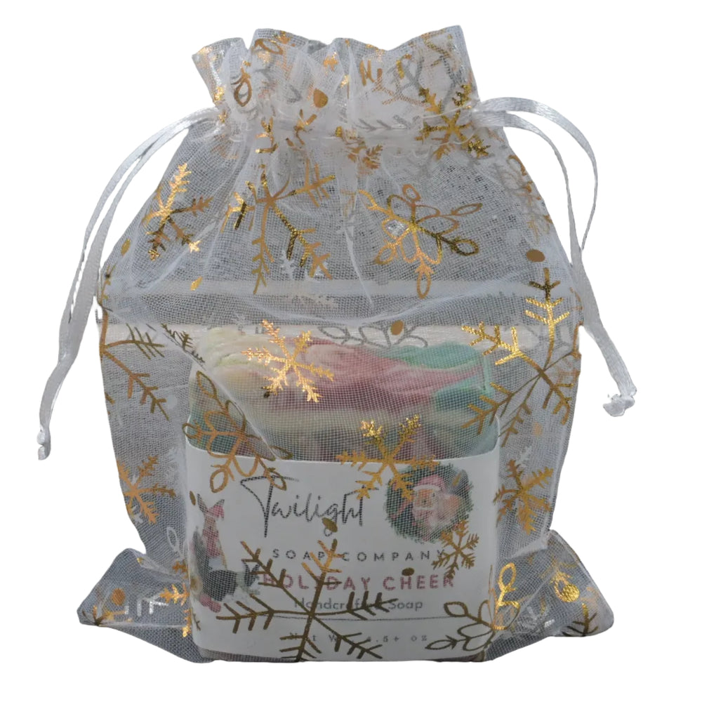 Clear drawstring bag with gold snowflake patterns containing a candle labeled 'Twilight' on a textured surface.