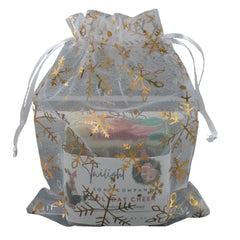 Clear drawstring bag with gold snowflake patterns containing a candle labeled 'Twilight' on a textured surface.